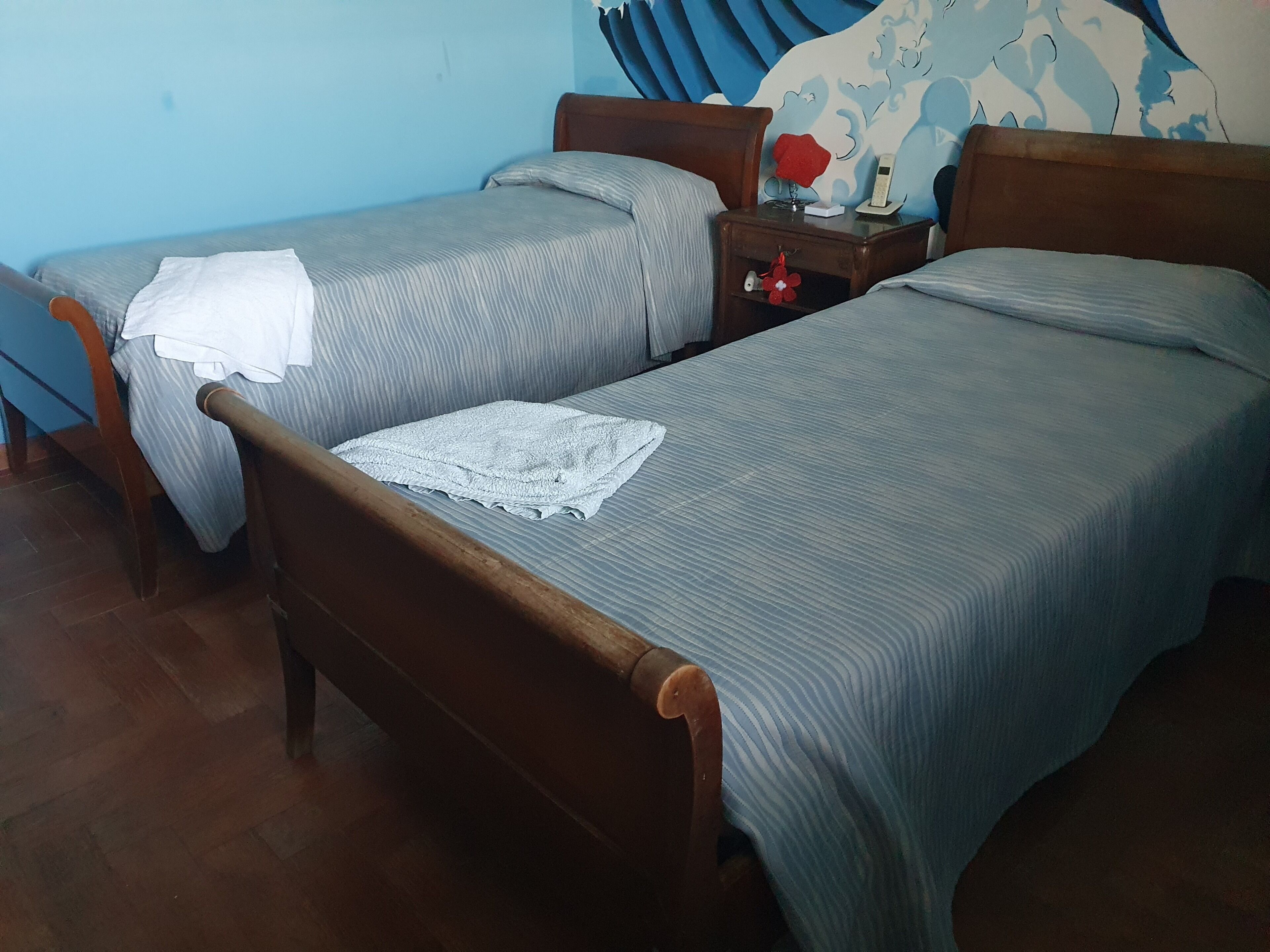 Ein Zimmer mit zwei Einzelbetten, einem Nachttisch aus Holz mit einem Telefon und einer Wand mit floralem Muster.