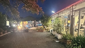 A paved outdoor area with potted plants, a building with glass windows, and a canopy structure. - AL RIFUGIO (Montecorvino Pugliano)