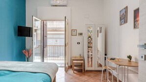 Een slaapkamer met een bed, een bureau en een stoel, een balkon met uitzicht en een deur naar een badkamer.