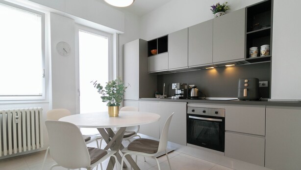 Una cocina moderna con armarios blancos, una mesa redonda con sillas y un horno empotrado.