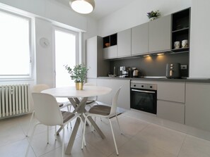 A modern kitchen with white cabinetry, a round dining table with chairs, and a built-in oven. - Mountain View Apartment Lecco Centro (Lecco)