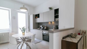 Una cocina moderna con armarios blancos, una mesa de comedor con sillas, una cafetera y un hervidor.