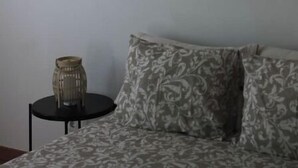 Een kamer met een bed, een wandlamp, een klein tafeltje met een decoratief object, en een wandkleed met een patroon.