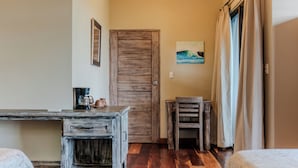 A room with a wooden door, a small table with a coffee pot, a chair, and a bed.