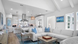 Un salon moderne avec un canapé blanc, une table basse et un coin repas doté de meubles blancs, et une cuisine en arrière-plan.