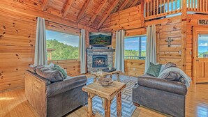 Een houten cabin met daarin twee banken, een open haard en een balkon met een 'Welcome'-bord.
