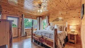Een slaapkamer in een houten chalet met een groot bed, een plafondventilator en uitzicht op de omgeving.