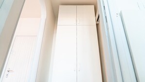 Un armario blanco con dos puertas y un tirador, situado en una habitación con paredes blancas y una puerta con líneas horizontales.