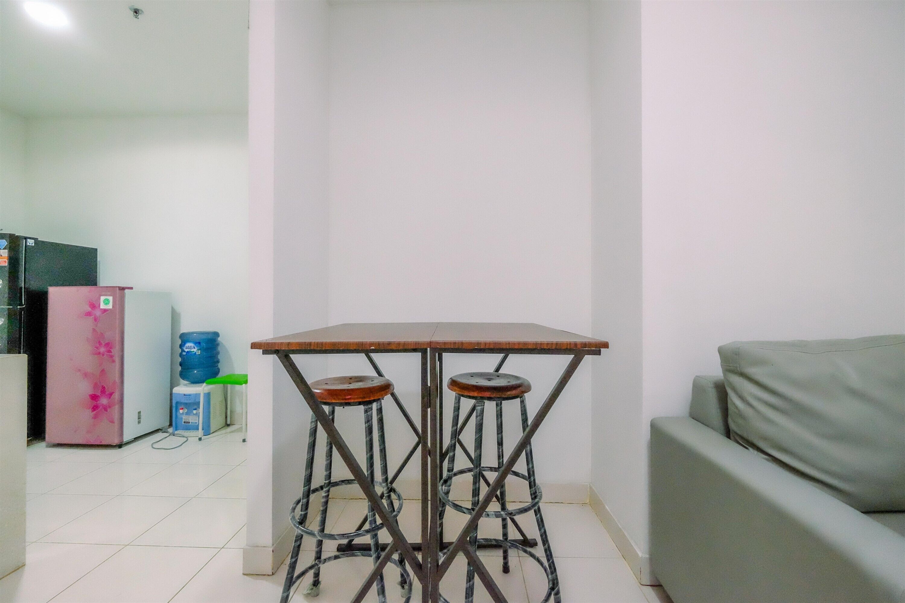 A small, clean room with a kitchenette, a grey sofa, and a table with two stools.