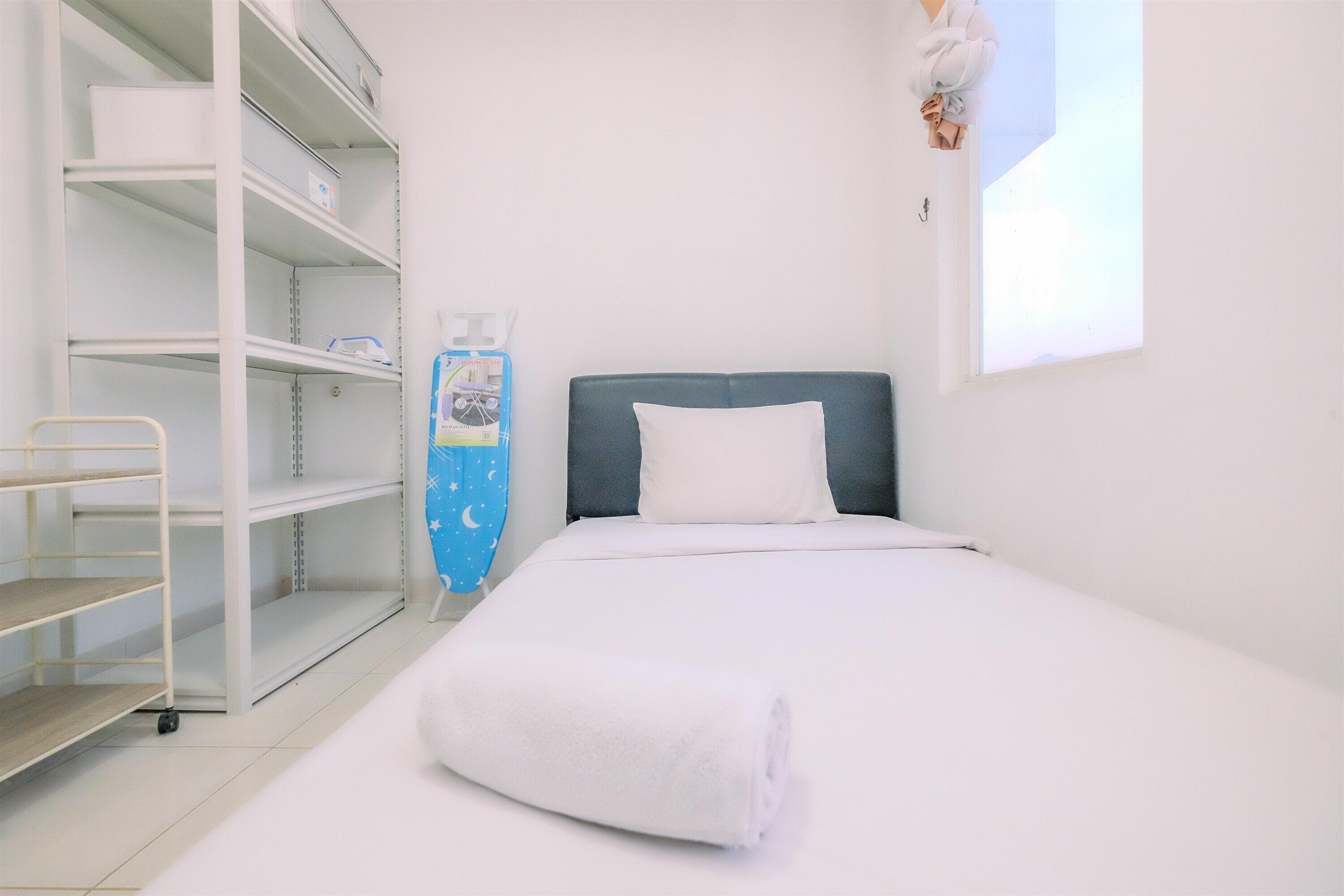 A hotel room with a bed, a white towel, a shelf unit, and a window.