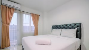 A hotel room with a large bed, a tufted headboard, and a window with curtains.