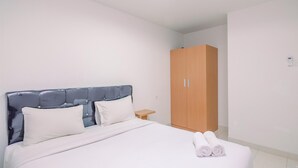 A neatly made bed with white linens and two pillows, a wooden wardrobe, and a small bedside table.