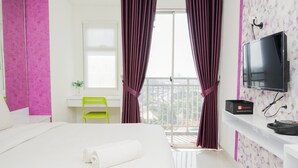 Habitación de hotel con cama, escritorio, silla, televisor y balcón con cortinas.