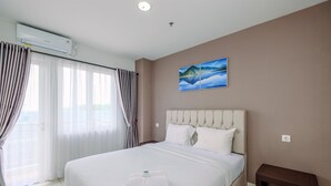 A hotel room with a large bed, a headboard, a bedside table, and a painting on the wall. - Comfort and Homey 2BR at Sentul Tower Apartment (Citaringgul)