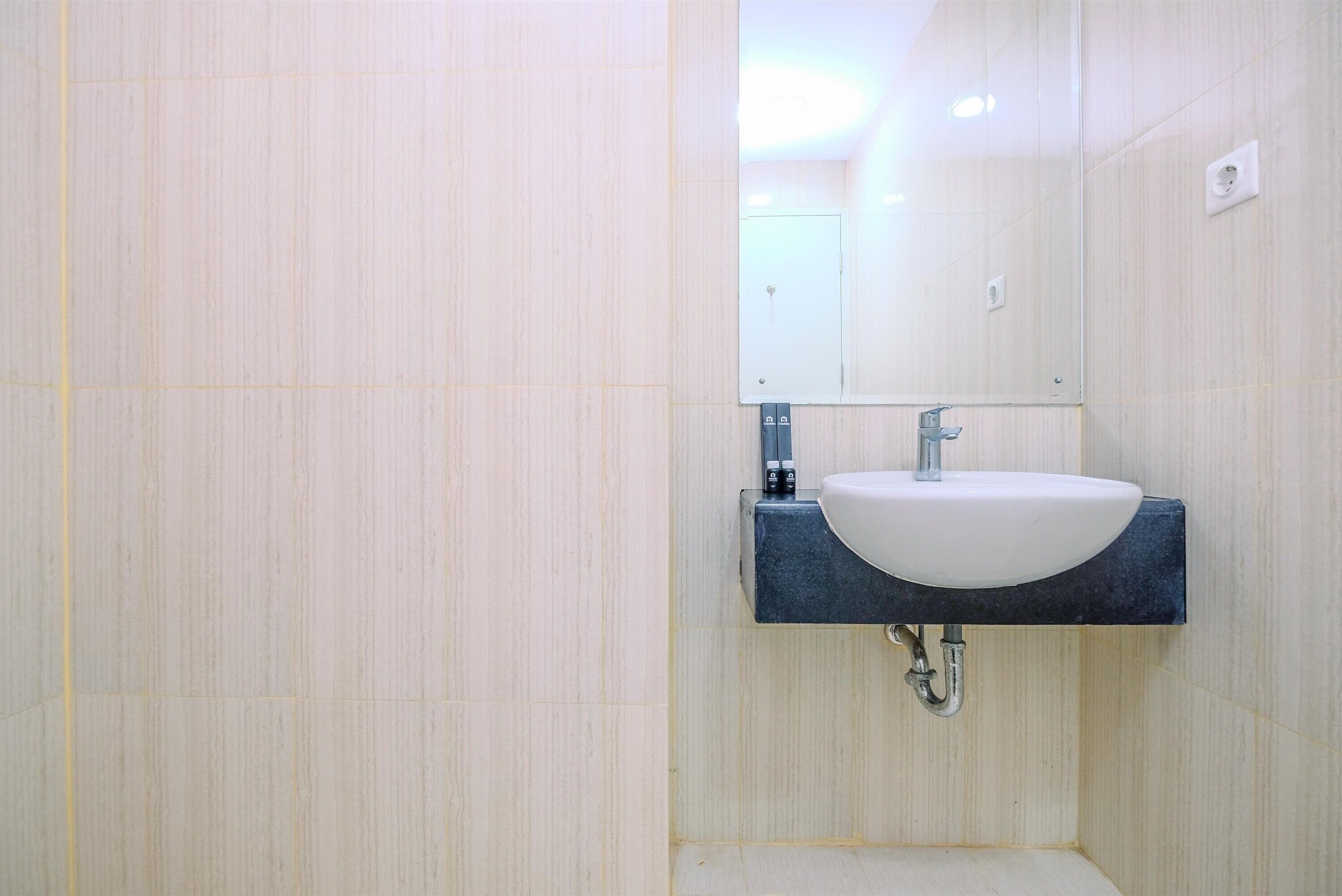 Un baño con un lavamanos blanco, encimera oscura y un espejo encima.