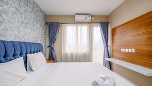 A hotel room with a large bed, a wooden headboard, a wall-mounted air conditioner, and a window with curtains. - Spacious 2BR at Sentul Tower Apartment (Citaringgul)