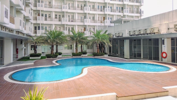 Ein modernes Apartmenthaus mit einem zentral gelegenen Schwimmbad, umgeben von Palmen und einer Holzterrasse.