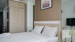 A hotel room with a bed, a wooden wardrobe, a television, and a cityscape picture on the wall. - Fancy and Nice Studio at Springwood Residence Tangerang Apartment (Tangerang)
