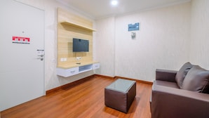 Una sala de estar moderna con un televisor de pantalla plana montado en un estante de madera, un sofá de cuero marrón, una mesa de centro de vidrio y una puerta blanca con un letrero rojo de salida de emergencia.