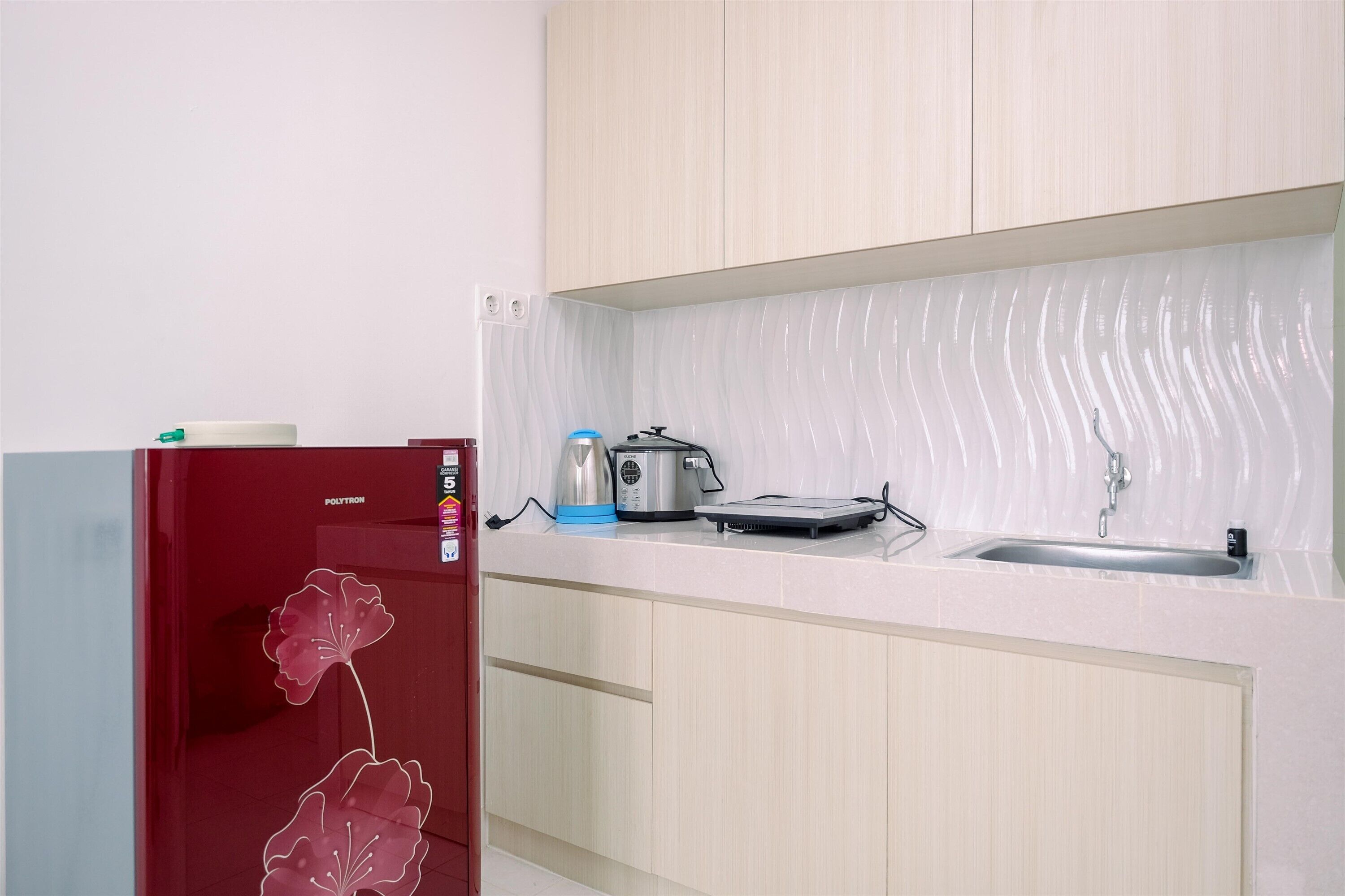 A compact kitchen with a refrigerator, a kettle, a toaster, and a sink.