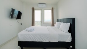 Et hotelværelse med en seng, et fjernsyn ophængt på væggen, en aircondition og et vindue med gardiner.
