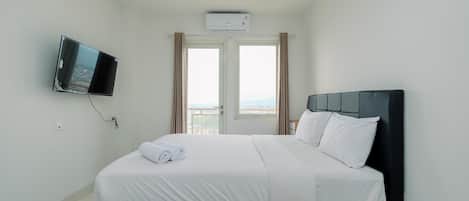 A hotel room with a bed, a television mounted on the wall, an air conditioning unit, and a window with curtains.