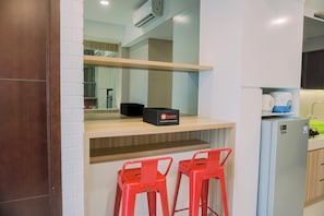 A compact kitchen with a wooden countertop, a black box labeled 'Travelio', a refrigerator, and two red bar stools. - Minimalist and Comfy 1BR Springwood Residence Tangerang Apartment (Tangerang)