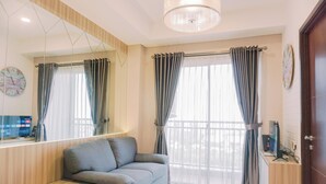 A modern living room with a sofa, a small table, a TV, and a large window with curtains. - Minimalist and Comfy 1BR Springwood Residence Tangerang Apartment (Tangerang)