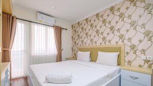 A neatly made bed with a white comforter and a folded towel, a wooden nightstand with a drawer, and a wall with a floral pattern. - Comfortable and Modern 2BR Sentul Tower Apartment (Citaringgul)