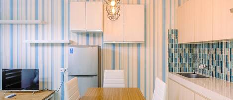 A compact kitchen with striped wallpaper, a wooden dining table, white chairs, a built-in fridge, and a tiled backsplash.