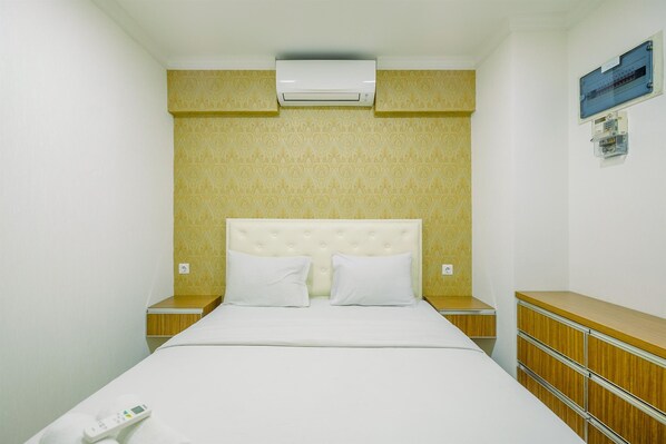A hotel room with a bed, a nightstand, a dresser, an air conditioning unit, and a wall-mounted control panel. - Comfort and Enjoy Living 2BR at Sentul Tower Apartment (Citaringgul)