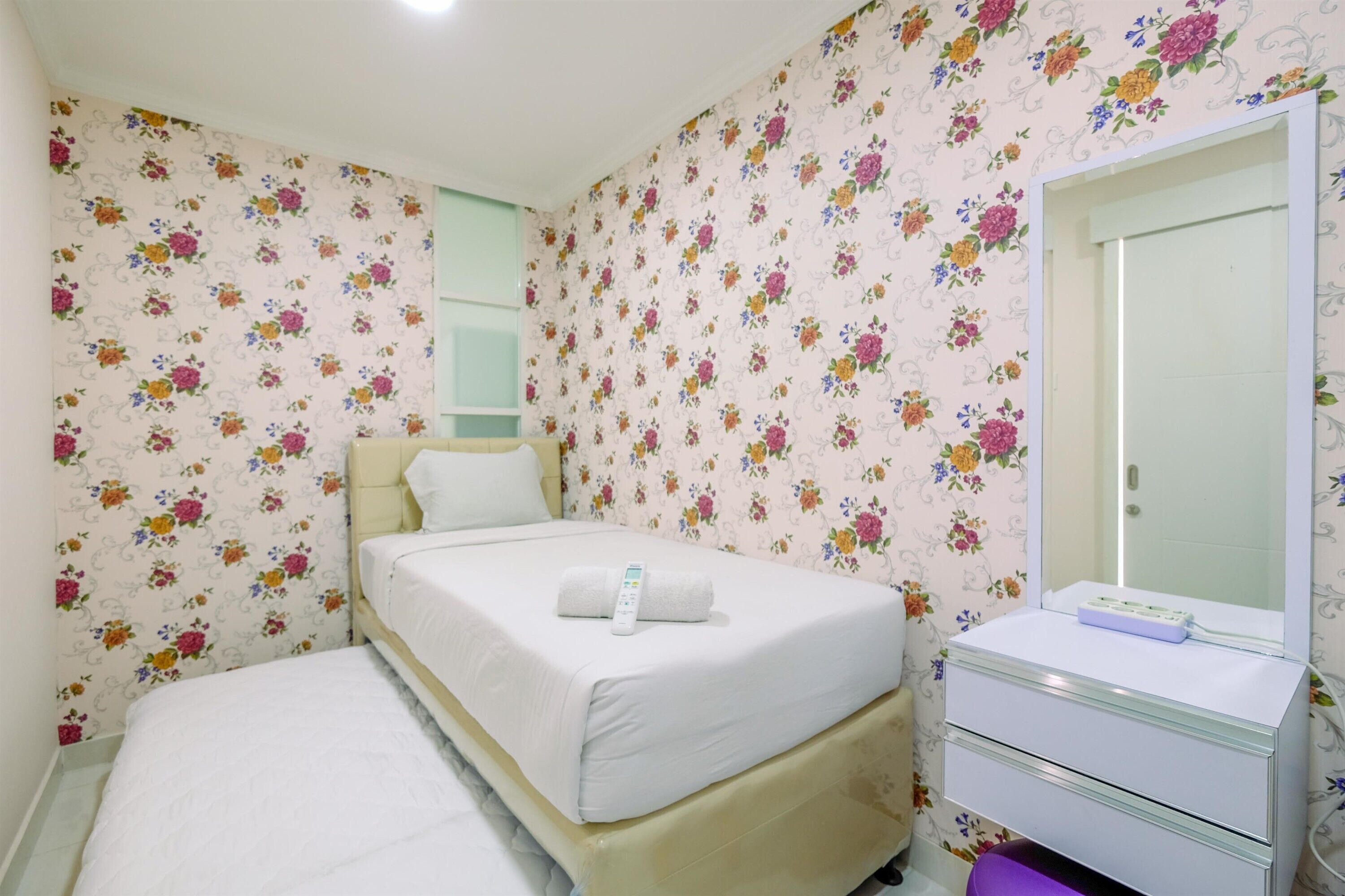 A hotel room with a bed, a bedside table, a mirror, and floral wallpaper.