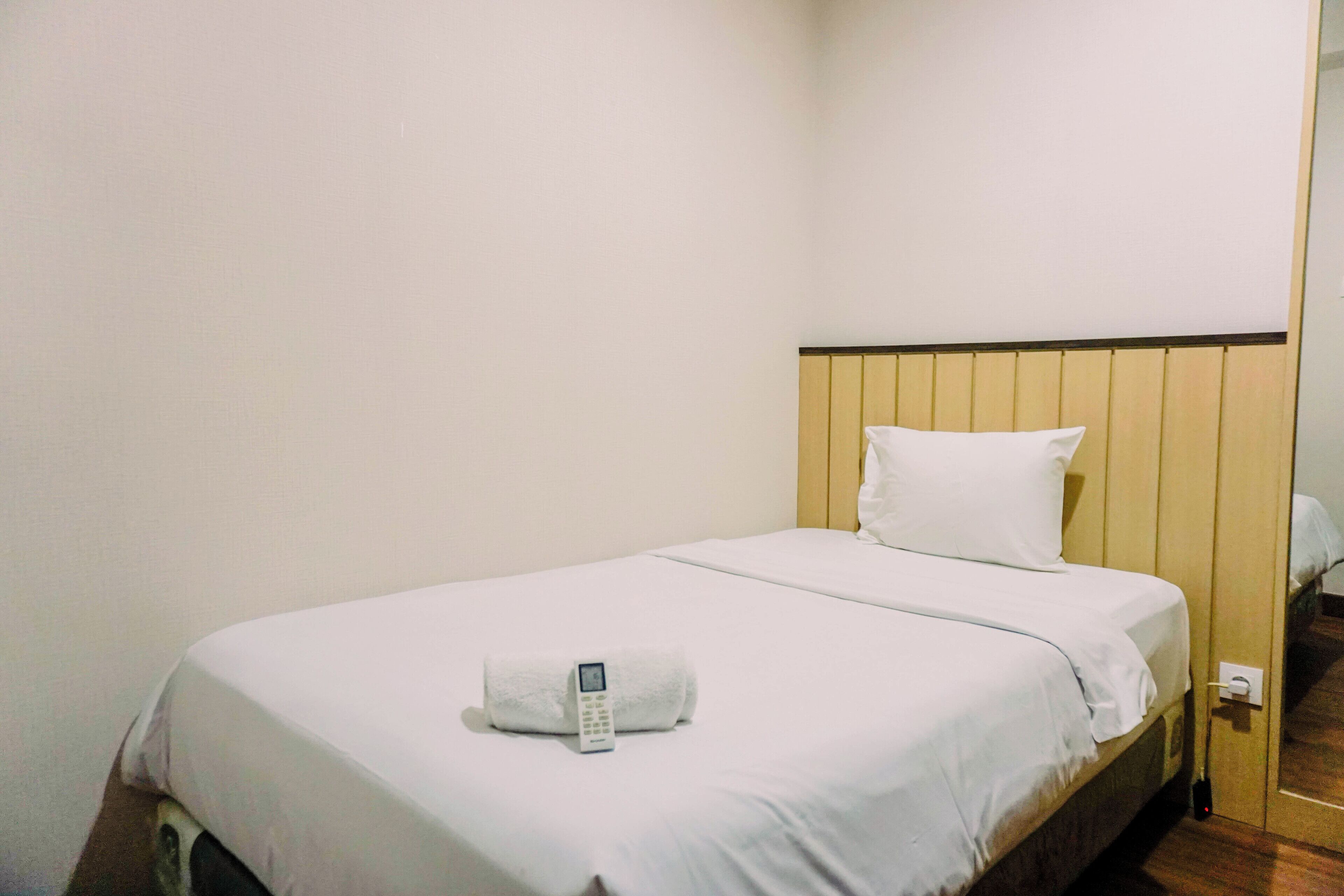 Hotelkamer met een enkel bed, een wit kussen, een witte deken en een witte handdoek, met een telefoon erop.