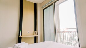 Une chambre d’hôtel avec un lit, une étagère contenant des articles de toilette, un tableau et une vue sur la ville par la fenêtre.