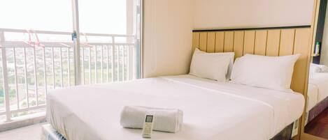 A hotel room with a large bed, a window with a view of buildings, and a balcony with chairs.