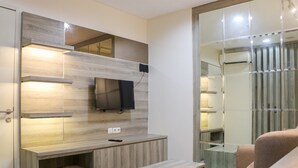 A modern living room with a built-in TV, wooden shelving, and a glass partition. - Fancy and Nice 2BR at Sentul Tower Apartment (Citaringgul)