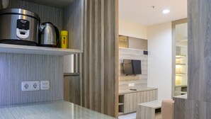 A modern kitchen with a stainless steel cooktop, a coffee maker, and a yellow bottle. There are wooden cabinets and a TV mounted on the wall. - Fancy and Nice 2BR at Sentul Tower Apartment (Citaringgul)
