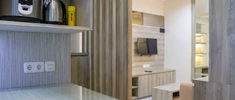 Una cocina moderna con una placa de cocina de acero inoxidable, una cafetera y una botella amarilla. Hay armarios de madera y un televisor montado en la pared.