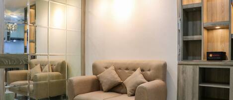 A modern living room with a beige sofa, a wooden cabinet, and a large mirror reflecting the room.
