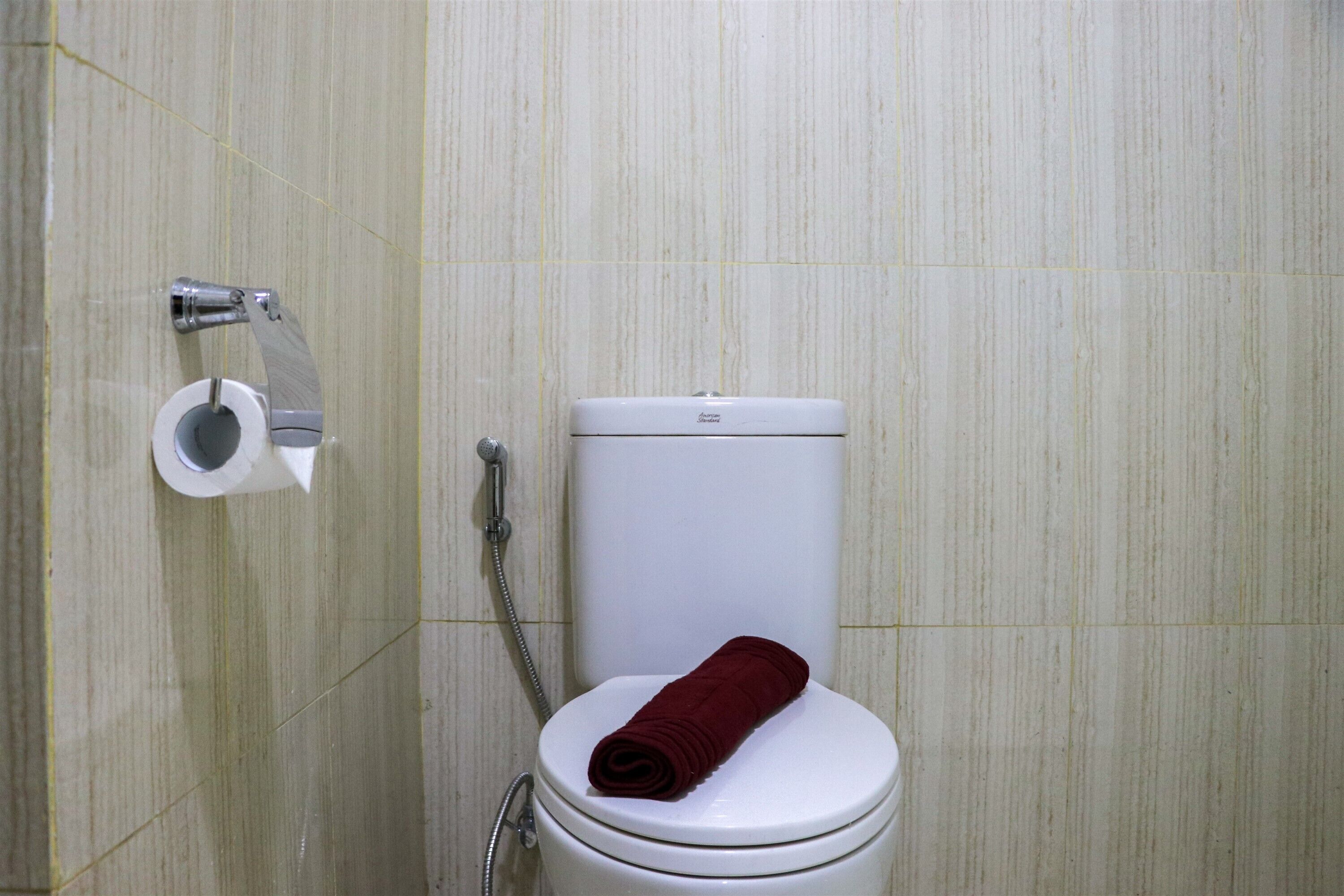 A bathroom with a toilet, a paper towel holder, and a shower head.