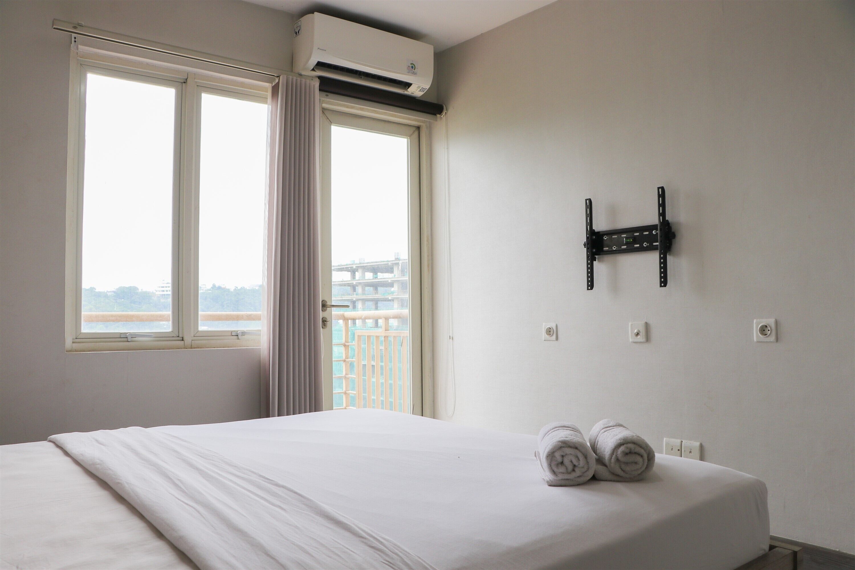 A hotel room with a bed, a window with curtains, an air conditioning unit, and a wall-mounted TV.