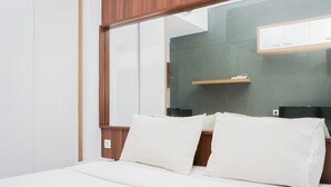 Ein modernes Hotelzimmer mit einem großen Bett, einem Holz-Kopfteil und einem Spiegel, der eine dunkle Wand und ein Regal mit einer Fernbedienung reflektiert.