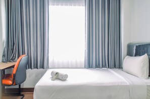 Hotellihuone, jossa on sänky, työpöytä, oranssi tuoli ja ikkuna, jossa on verhot.