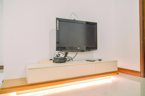 A flat-screen TV mounted on a wall above a white cabinet with a remote control and a small speaker on it.
