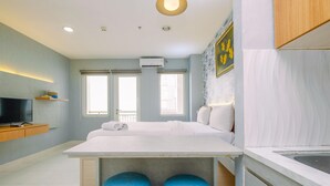 A modern hotel room with a large bed, a small kitchen area, and a TV on a wooden shelf. - Cozy Studio at Sentul Tower Apartment (Citaringgul)
