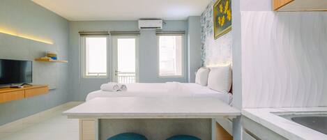 Habitación de hotel moderna con una cama grande, una pequeña cocina y un televisor sobre una estantería de madera.