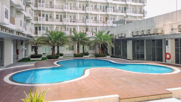 A modern apartment building with a central swimming pool surrounded by palm trees and a wooden deck. - Cozy Studio at Sentul Tower Apartment (Citaringgul)