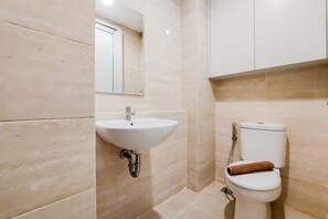 Un baño con lavamanos blanco, inodoro y una toalla enrollada sobre el asiento del inodoro.