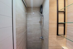 Une petite douche avec une étagère en verre et un pommeau de douche à main.