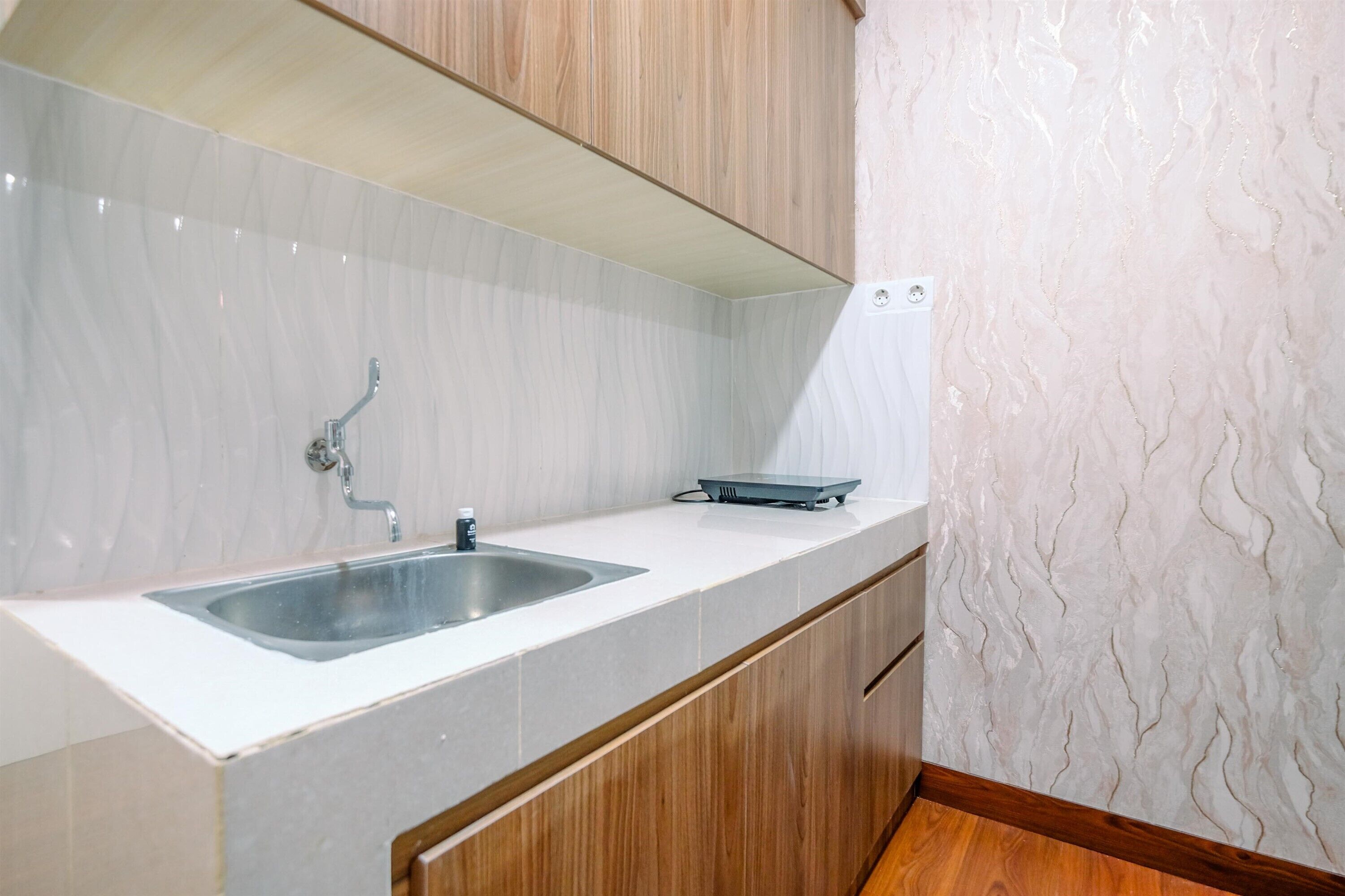 Una cocina moderna con encimera blanca, pileta de acero inoxidable y alacenas de madera.